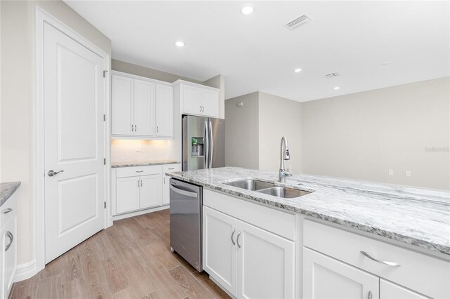 kitchen featuring light wood-type flooring, appliances with stainless steel finishes, light stone countertops, sink, and white cabinets