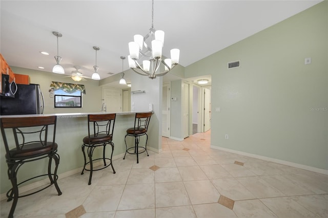 kitchen with ceiling fan with notable chandelier, vaulted ceiling, a breakfast bar, pendant lighting, and appliances with stainless steel finishes