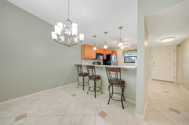 kitchen featuring kitchen peninsula, a kitchen breakfast bar, ceiling fan with notable chandelier, backsplash, and stainless steel fridge