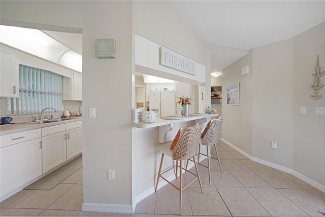 kitchen featuring light tile patterned flooring, sink, a kitchen breakfast bar, white refrigerator with ice dispenser, and white cabinets