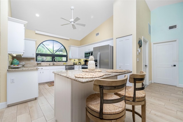 kitchen with sink, appliances with stainless steel finishes, high vaulted ceiling, a kitchen island, and white cabinets