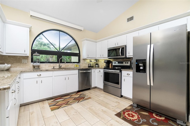 kitchen with stainless steel appliances, vaulted ceiling, decorative backsplash, sink, and white cabinetry