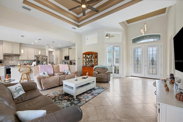 living room with french doors, light tile patterned floors, ceiling fan, crown molding, and a high ceiling