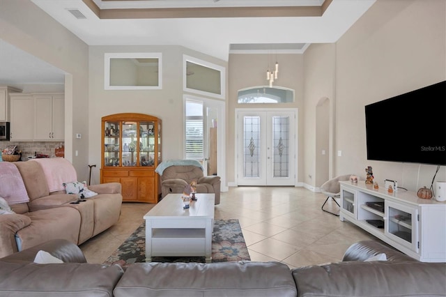 living room featuring french doors, light tile patterned flooring, a raised ceiling, a high ceiling, and a chandelier