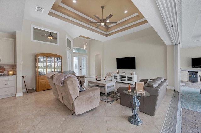 living room featuring french doors, crown molding, beverage cooler, a tray ceiling, and ceiling fan