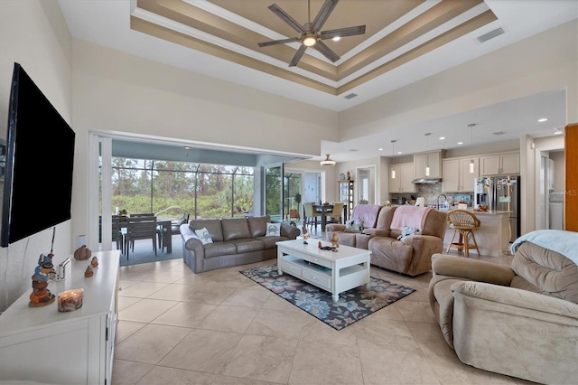 living room with ornamental molding, a high ceiling, ceiling fan, and a raised ceiling