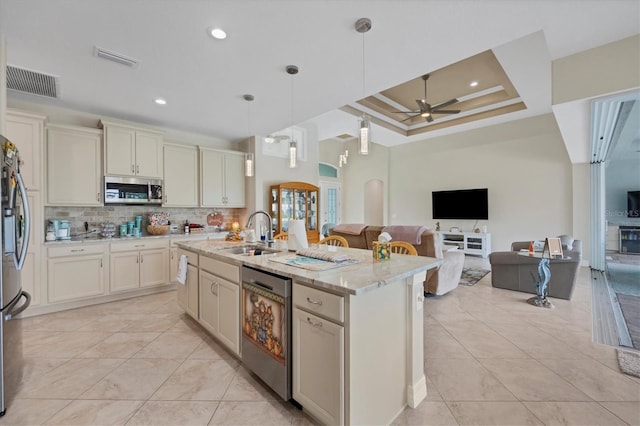 kitchen with sink, appliances with stainless steel finishes, light stone countertops, ceiling fan, and an island with sink