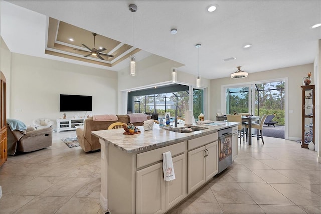 kitchen with sink, light stone countertops, ceiling fan, hanging light fixtures, and a kitchen island with sink