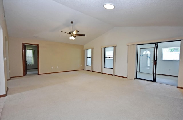 empty room with ceiling fan, plenty of natural light, light carpet, and lofted ceiling