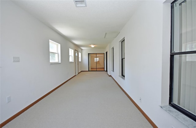 hall with a textured ceiling and light colored carpet