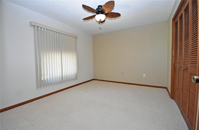 unfurnished bedroom featuring a closet, a textured ceiling, light colored carpet, and ceiling fan