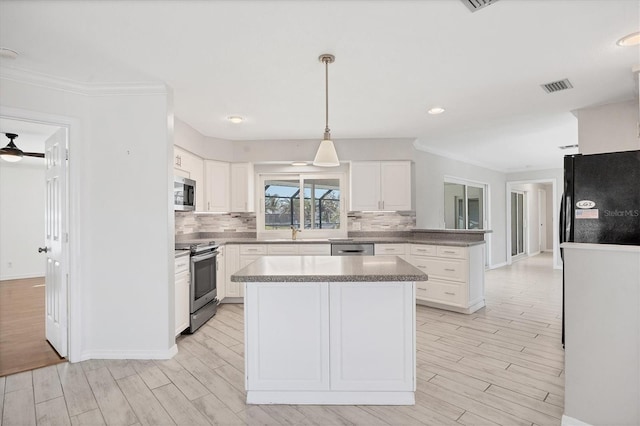 kitchen with a kitchen island, appliances with stainless steel finishes, pendant lighting, white cabinetry, and light hardwood / wood-style floors