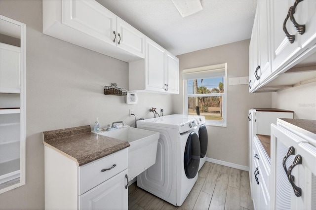 laundry room with sink, cabinets, a textured ceiling, light wood-type flooring, and washer and clothes dryer