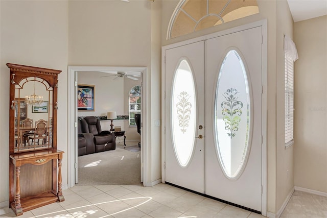 entryway with a towering ceiling, ceiling fan with notable chandelier, and light carpet