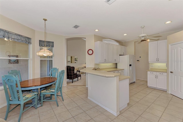 kitchen with kitchen peninsula, white refrigerator with ice dispenser, ceiling fan, white cabinetry, and decorative light fixtures