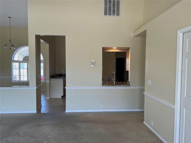 unfurnished room with dark colored carpet, a towering ceiling, an inviting chandelier, and sink