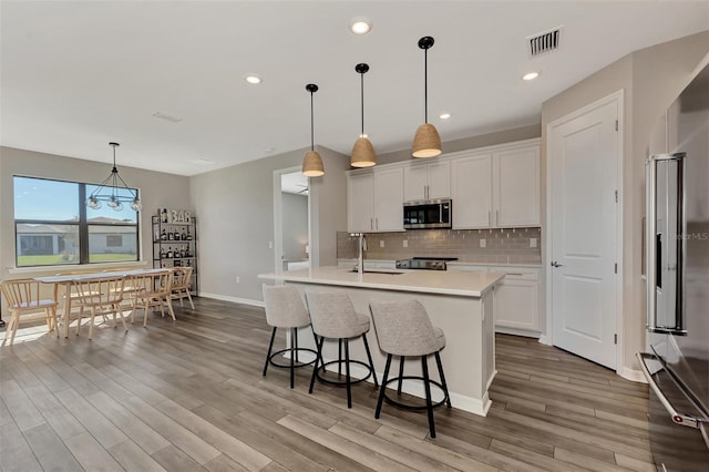 kitchen featuring white cabinetry, appliances with stainless steel finishes, an island with sink, and hanging light fixtures