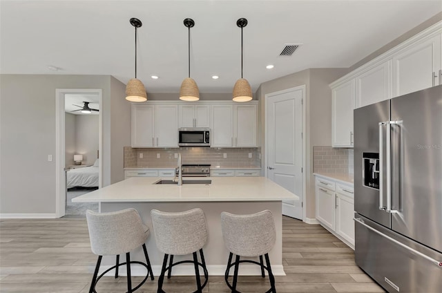 kitchen featuring stainless steel appliances, white cabinets, a center island with sink, and pendant lighting