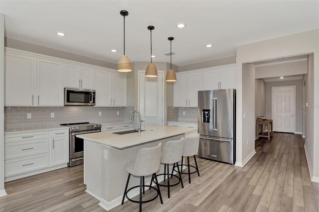 kitchen with light hardwood / wood-style floors, sink, appliances with stainless steel finishes, a kitchen island with sink, and white cabinets