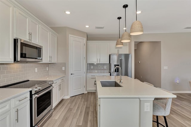 kitchen featuring white cabinets, a center island with sink, appliances with stainless steel finishes, and sink