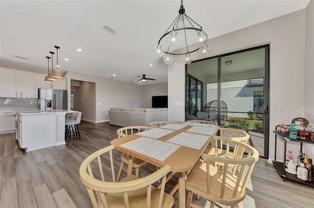 dining area with ceiling fan with notable chandelier, sink, and light hardwood / wood-style flooring