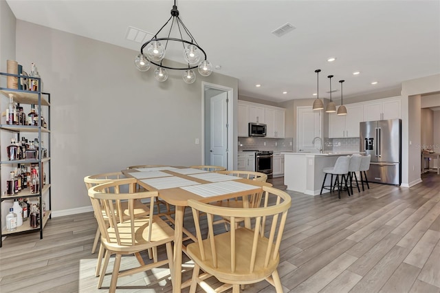 dining space featuring an inviting chandelier, sink, and light wood-type flooring