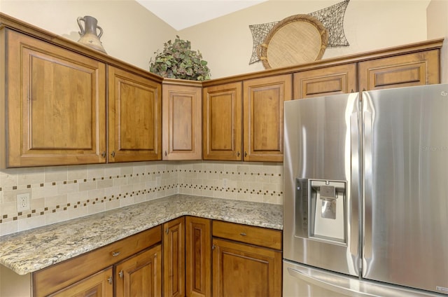 kitchen with tasteful backsplash, light stone counters, and stainless steel fridge