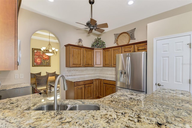 kitchen with tasteful backsplash, light stone countertops, stainless steel refrigerator with ice dispenser, sink, and ceiling fan with notable chandelier