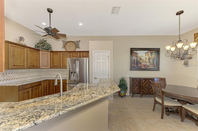 kitchen featuring light stone countertops, light tile patterned floors, decorative light fixtures, stainless steel fridge, and decorative backsplash