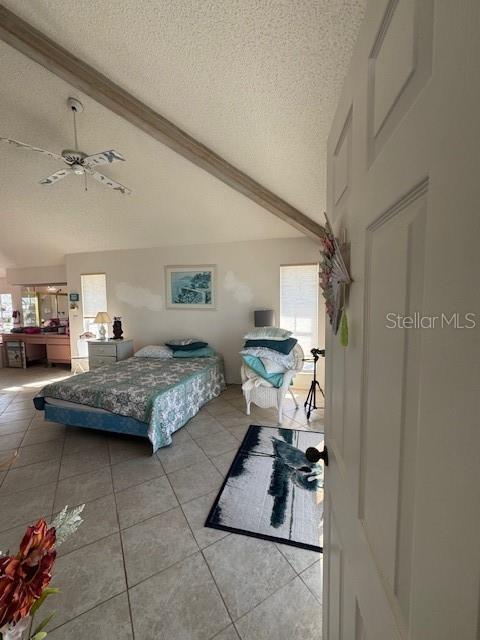 tiled bedroom with a textured ceiling, lofted ceiling with beams, multiple windows, and ceiling fan