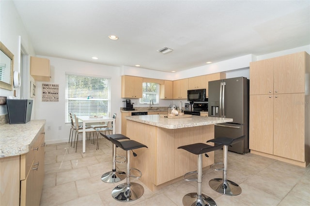 kitchen featuring stainless steel refrigerator with ice dispenser, light brown cabinetry, a breakfast bar, sink, and a kitchen island