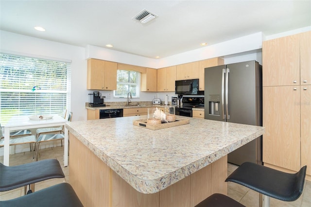 kitchen featuring a center island, light brown cabinets, a kitchen breakfast bar, light tile patterned floors, and black appliances