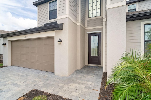 doorway to property with a garage, driveway, and stucco siding