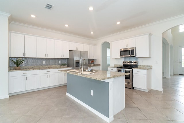 kitchen with stainless steel appliances, white cabinetry, a center island with sink, light stone counters, and ornamental molding