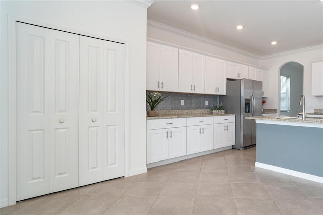 kitchen with crown molding, white cabinetry, light tile patterned floors, stainless steel refrigerator with ice dispenser, and sink