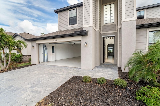 property entrance featuring a shingled roof, decorative driveway, an attached garage, and stucco siding