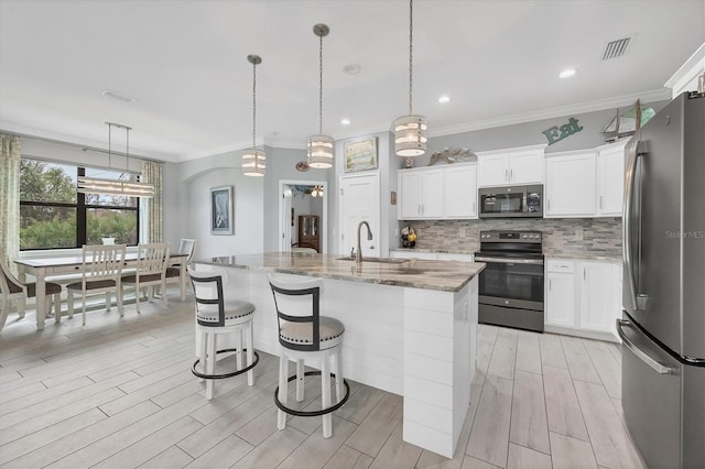 kitchen featuring an island with sink, light stone countertops, decorative light fixtures, and appliances with stainless steel finishes