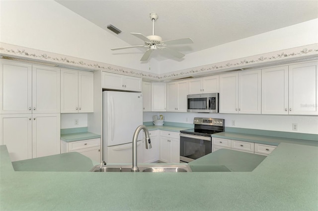 kitchen with stainless steel appliances, vaulted ceiling, ceiling fan, sink, and white cabinetry