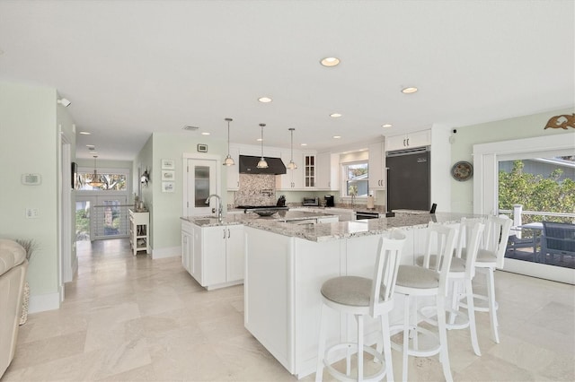 kitchen with exhaust hood, white cabinets, built in refrigerator, a large island, and light stone counters