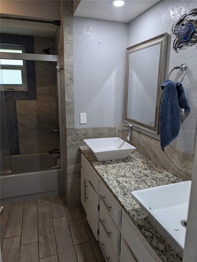705 Chevy Chase St NW, Port Charlotte, FL 33948 - bathroom featuring bath / shower combo with glass door, double vanity, wood finish floors, a textured wall, and tile walls