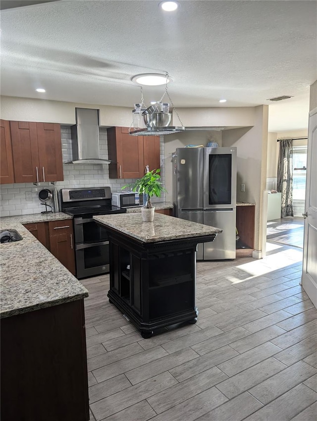 kitchen with light stone countertops, decorative backsplash, wall chimney exhaust hood, stainless steel appliances, and a kitchen island