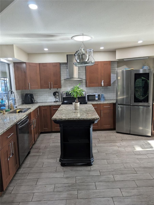 kitchen featuring light stone countertops, stainless steel appliances, sink, wall chimney range hood, and a kitchen island