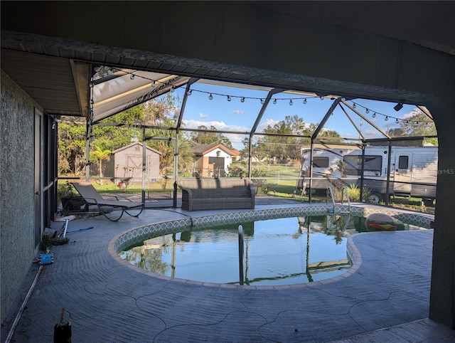 view of pool featuring glass enclosure, a patio area, and a storage shed