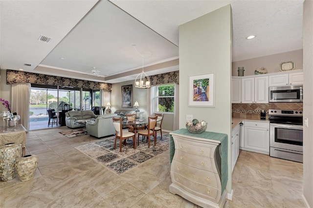 kitchen with ceiling fan with notable chandelier, a textured ceiling, tasteful backsplash, white cabinetry, and appliances with stainless steel finishes