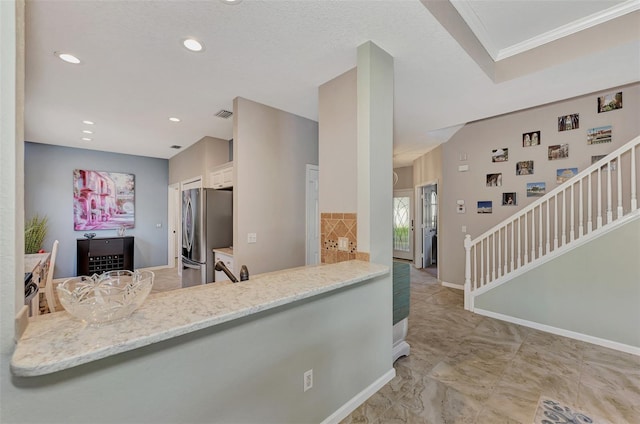 kitchen with light stone counters, white cabinets, kitchen peninsula, sink, and stainless steel refrigerator