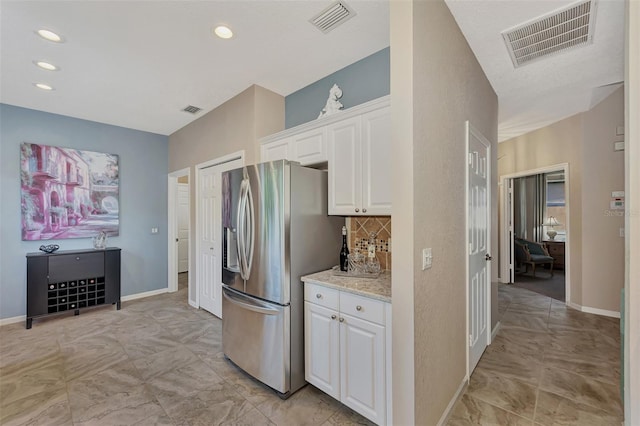 kitchen featuring light stone countertops, stainless steel refrigerator with ice dispenser, white cabinetry, and backsplash