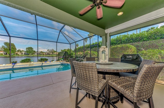 view of swimming pool with a patio, ceiling fan, glass enclosure, and a water view