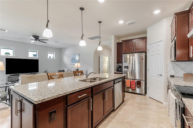 kitchen with appliances with stainless steel finishes, ceiling fan, a kitchen island with sink, sink, and decorative light fixtures