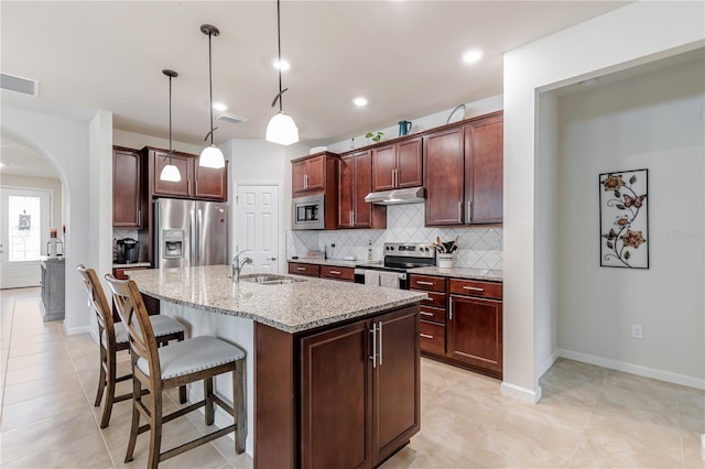 kitchen featuring light stone countertops, sink, stainless steel appliances, decorative light fixtures, and a center island with sink