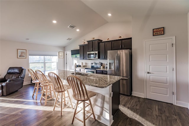 kitchen featuring stainless steel appliances, dark hardwood / wood-style flooring, light stone countertops, an island with sink, and a breakfast bar area